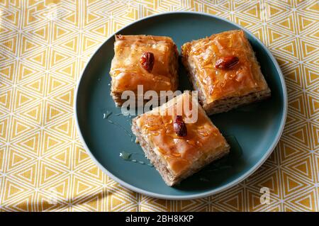 Oriental kitchen, sweets, homemade bakery, turkish baklava with walnuts and orange sirup on green plate and tea towel. Stock Photo