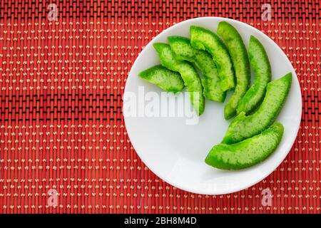 Green slices of exotic candied fruit on white plate. Succade of pomelo on bright wicker tablecloth. Confectionery top view. Vegetarian food background Stock Photo