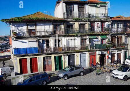 Picturesquely decaying row of old three & four storey residential buildings with multi-coloured front doors and iron balustraded balconies, in Porto Stock Photo