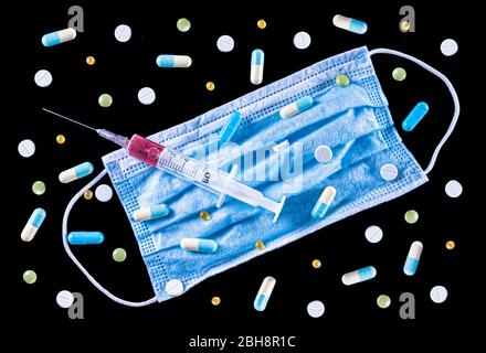 Flat Lay of blue surgical face mask, medical plastic 5 ml syringe filled with red liquid (blood) and various colorful pills, tablets and capsules on a Stock Photo