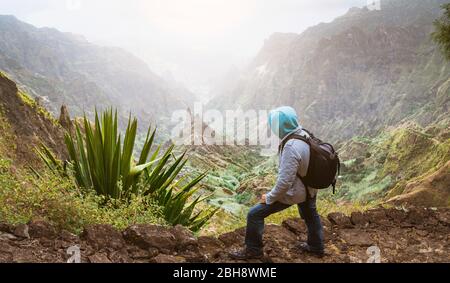 Traveler with backpack looking over the rural landscape with mountain peaks and ravine in dust air on the path from Xo-Xo Valley. Santo Antao Island, Cape Verde. Stock Photo