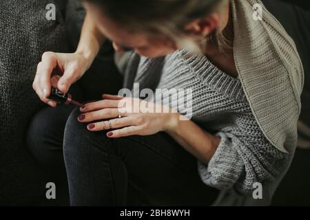Frau sitzt entspannt auf der Couch, lackiert sich die Fingernägel