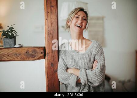 junge Frau in ihrer Wohnung, Arme verschränkt, lachen, Halbporträt