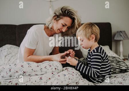 Morgens im Bett, Mutter verarztet Wunde am Finger ihres Sohnes Stock Photo