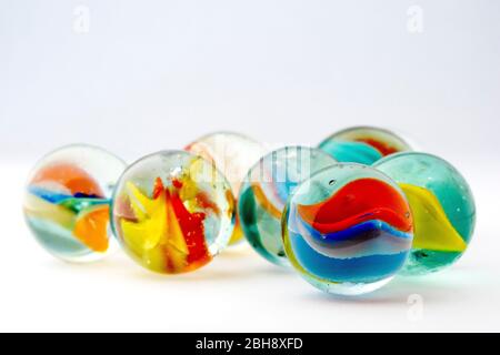 Close up still life of several colourful glass marbles shot against a white background.