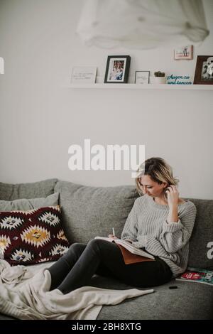 Frau mit Notizbuch und Zeitschrift auf der Couch Stock Photo