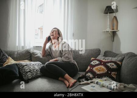 Frau telefoniert fröhlich auf der Couch