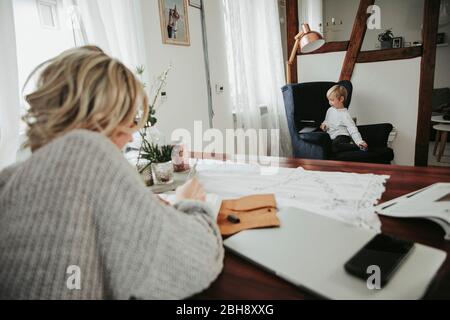 Frau mit Laptop und Notizbuch, Sohn spielt mit Tablet Computer im Hintergrund Stock Photo