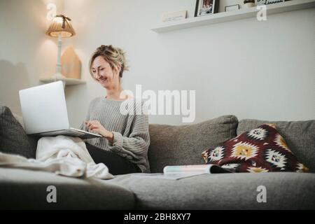 Frau sitzt entspannt mit Laptop auf der Couch, glücklich, lächeln Stock Photo