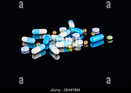 Different tablets, pills and capsules of different colors on an isolated black background with reflection Stock Photo