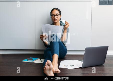 Woman looking on documents while drinking coffee at kitchen counter Stock Photo