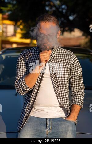Young man standing next to car while vaping Stock Photo