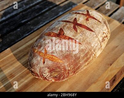 Freshly baked sourdough bread on butcher block cutting board outside Stock Photo