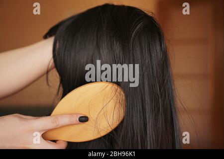 Female hand holds a black wig with long hair and combs a wooden comb. Hairdresser and hair care Stock Photo