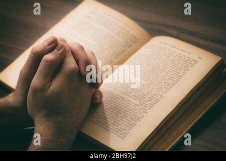 Prayer, man hands over an open book Holy Bible, wooden desk background. Faith, religion and spirituality concept Stock Photo