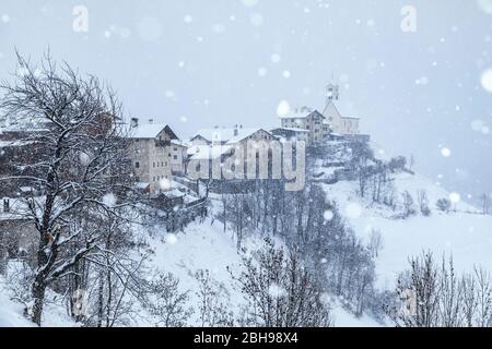 the ancient village of Colle Santa Lucia with the church on the hill under a snowfall, agordino, belluno, veneto, italy Stock Photo