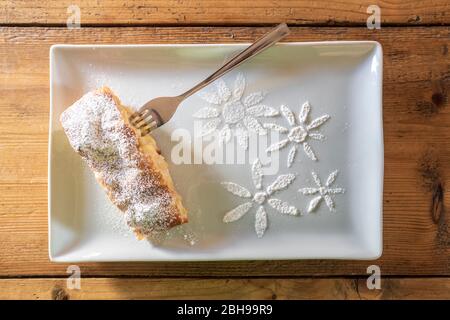 Delicious slice of apple strudel with powdered sugar and sugar decoration on a wooden table, typical dessert of the Dolomites and South Tyrol, Italy Stock Photo