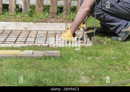 Low angle view of man making a net of steel bars as a reinforcement in a hole for a concrete foundation outside in backyard. Stock Photo