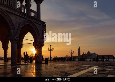 Doge's Palace on St. Mark's Square with romantic lovers in the backlight to the sunrise in the background San Giogio Maggiore and the Bacino di San Marco in between