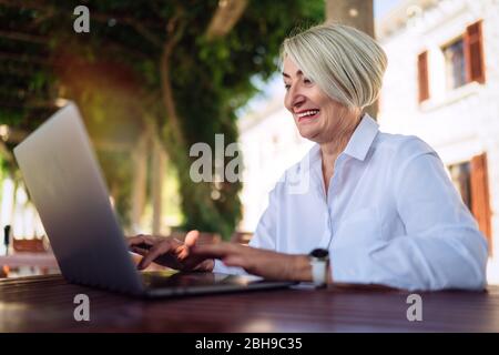 Confident senior woman typing text on a laptop computer in a cafe
