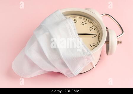 Medical disposable mask on an alarm clock on a pink background close-up. The concept of quarantine and the Countdown to the financial crisis due to co Stock Photo