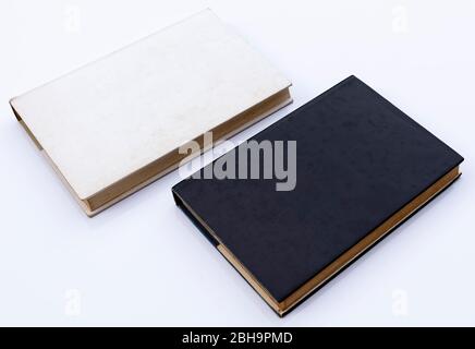 wo old hardcover paper books, one white and the other black, are placed against a white background Stock Photo