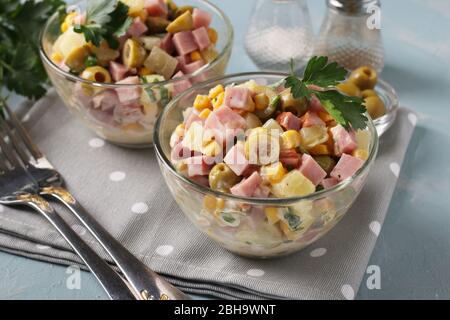 Salad with ham, olives, corn and pineapples in transparent salad bowls on a light blue background, Closeup Stock Photo