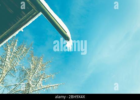 A rain gutter on the roof of a house in winter with snow and ice. Stock Photo
