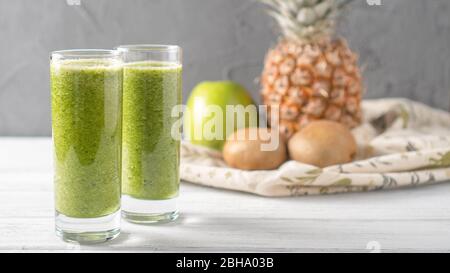 Refreshing green superpower summer drink. Pineapple kiwi apple smoothie on gray background with fruits behind. Stock Photo