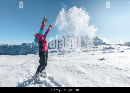 9 years old girl plays throwing snow in the air in Laresei hut, in front of the Pale di San Martino, Falcade, Dolomites, Belluno, Veneto, Italy Stock Photo