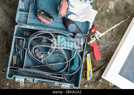 Toolbox with an electric hammer drill, headphones, glasses, next to it is a professional spray gun for foam and a PVC window. Stock Photo