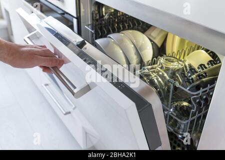 Man hand opens the dishwasher with clean dishes in it after washing. Stock Photo