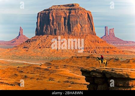 Cowboy on horse on cliff in desert landscape with butte rock formations, Monument Valley, Utah, USA Stock Photo