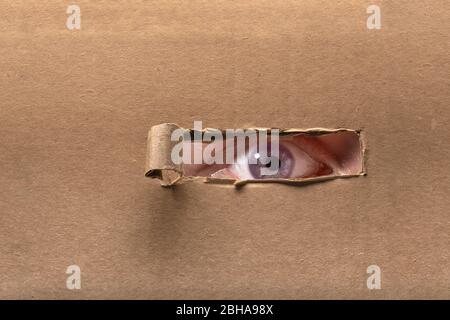 Eye peeking through torn paper Stock Photo