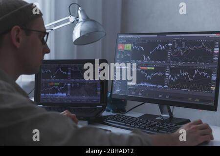 Thoughtful serious trader broker analyzing stock market graphs at pc and laptop. Stock Photo