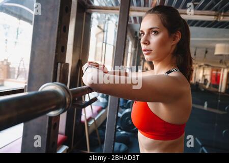 Attractive young fit sportswoman standing in the gym, resting after exercises, leaning on a rail Stock Photo