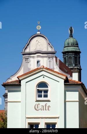 Germany, Bavaria, Upper Bavaria, Altötting, St. Anna's Basilica, church tower with statue of Mary and baby Jesus, front facade with relief image of the patron saint of St. Anne with Mary and baby Jesus, in the foreground a cafe Stock Photo