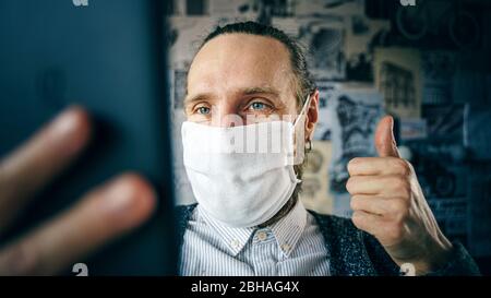 Portrait of a bearded man in a gauze mask, who talking remotely using tablet via video conference. Remote communication during an epidemic concept. Stock Photo