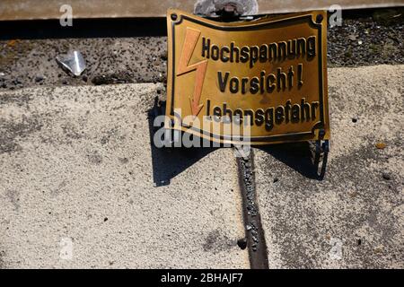 A dented and rusted warning sign with the note: Caution high voltage. Stock Photo