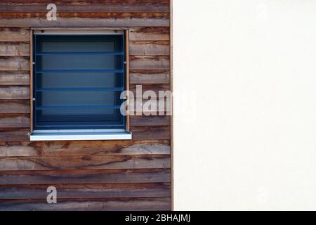 The exterior facade of a residential building with a small window in the wood paneling. Stock Photo