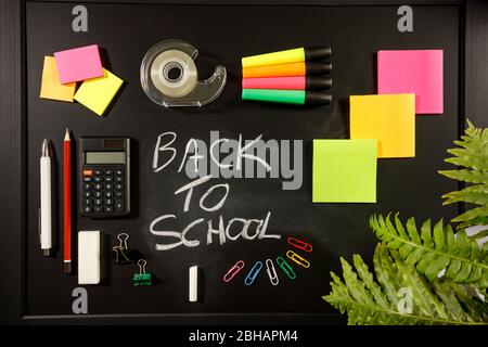 back to school concept on black flat lay, back to school written with chalk on blackboard with stationery, calculator, sticky notes, pen, pencil, tape Stock Photo