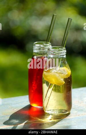 Two small glass bottles with homemade lemon and elderberry lemonade on a garden table Stock Photo