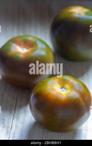 fresh kumato tomato fruit vegetable, also called black tomato, on old worn wooden board with back light Stock Photo