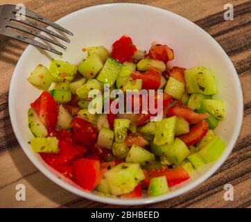 Juicy salad of tomatoes and cucumbers prepared with spices in a white bowl on a wooden table Stock Photo