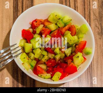 Top view of juicy salad of tomatoes and cucumbers prepared with spices in a white bowl with a fork on left side Stock Photo