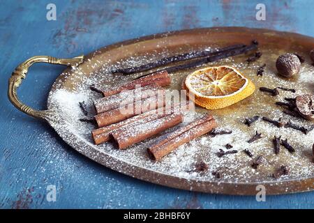Cinnamon and vanilla sticks, dried orange, nutmeg and cloves on metal tray on color wooden background Stock Photo