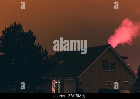 Pink smoke over roof during night time. Pink Orange color by illumination of greenhouses. Light pollution in The Netherlands. Stock Photo