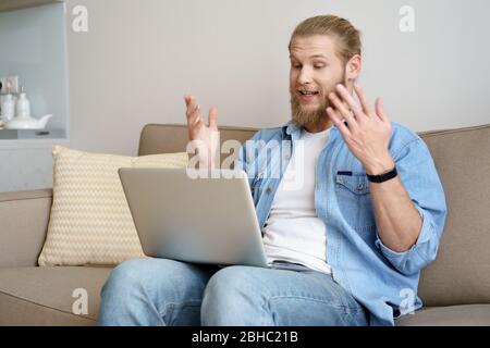 Young man video calling on laptop sit on sofa working from home office. Stock Photo