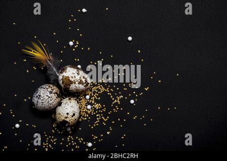 Moody easter decor. Quail eggs and feathers on black background. Happy easter holiday. Stock Photo