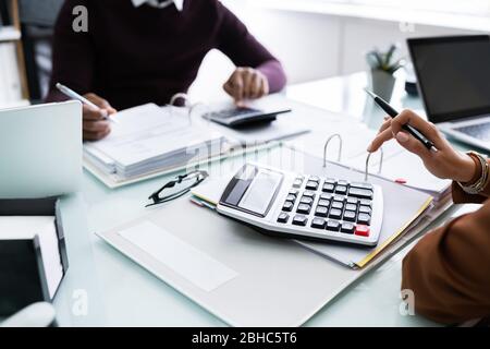 Close-up Of Two Businesspeople Calculating Financial Statement At Desk Stock Photo